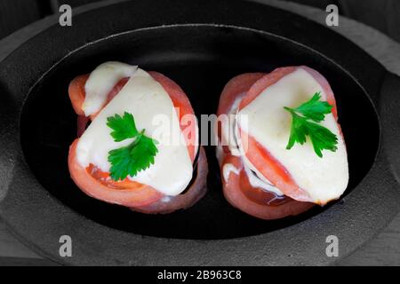 Baked eggplant with tomato, cheese and cilantro leaf in cast iron portion pan on wooden cooking board. Selective color effect. Stock Photo