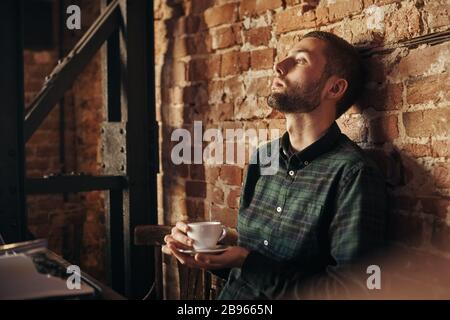 man writing on an old typewriter. In the meantime, he drinks coffee Stock Photo