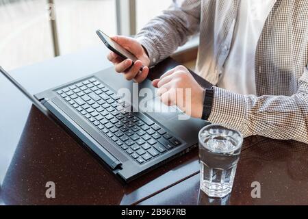 Remote work. Man using laptop, holding smart phone for business work or study, smart watch. Freelancer work space, employee on telework. Close up Stock Photo