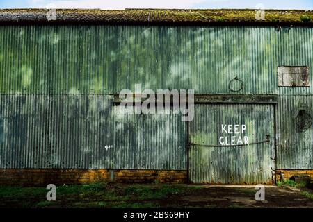 The words Keep Clear roughly painted on a weathered painted corrugated wall on the side of a shed Stock Photo
