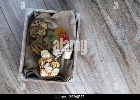 Cocoa with marshmallows and chocolate baking and slices of chocolate and jelly candies stand in wooden box on wooden table Stock Photo