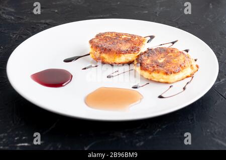 Cottage cheese pancakes on a plate are decorated with honey with blueberries, honey with strawberries and carob syrup. Healthy and diet Breakfast. Stock Photo