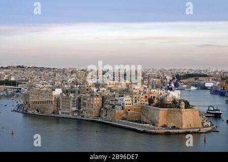 View of the Grand Harbour and Senglea, Malta from Valletta at dusk. The landmark watchtower (vedette) in Gardjola Gardens is in the right foreground. Stock Photo