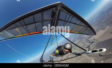 Hang glider pilot with his colorful wing flies alone far from other people. Concept of self isolation and social distance in the wild nature. Stock Photo