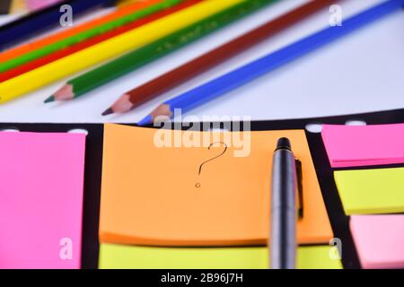 Question mark written by pen on colored stickers on the table, pen and colored pencils lie near Stock Photo
