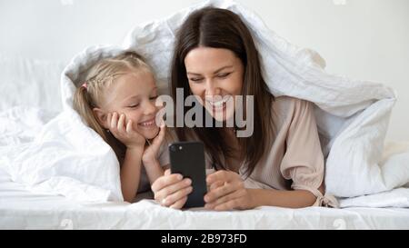Happy mom and daughter watch cartoon under blanket Stock Photo