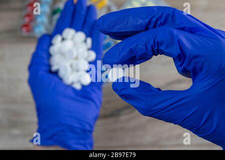 Many small white pills in the hands of a doctor wearing medical blue disposable gloves. Hands take one pills Stock Photo