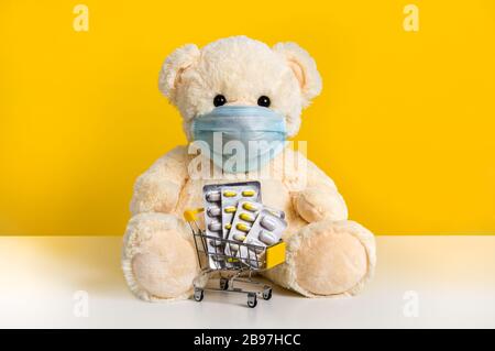 Teddy bear in medical mask with shopping cart with medicine: blister packs of pills. Concept of pediatrics, hygiene, virus protection and shopping for Stock Photo