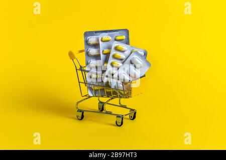 Shopping cart loaded with blister packs of pills on yellow background. Creative concept of healthcare and safe online shopping for medicine at pharmac Stock Photo