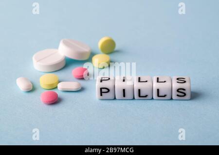 Word Pills made of white cubes and different pills on a blue medical background. To get sick, take pills or undergo treatment concept. Health care. Stock Photo
