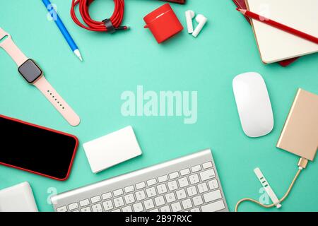 keyboard, golden power bank with cable, red smartphone with blank black screen, headphones, blank paper business cards and wireless mouse on green bac Stock Photo