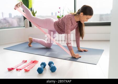 Resistance band fitness at home Asian woman doing leg workout donkey kick floor exercises with strap elastic. Glute muscle activation with kickback Stock Photo