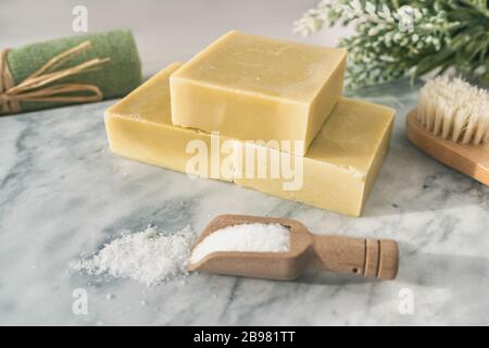 Handmade natural soap bars with epsom salt and scrubbing towel for skincare exfoliation spa therapy. Top view of olive oil soaps on marble background Stock Photo