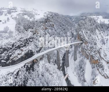 Aerial View of the Landwasser Viaduct with Railway without famous train at winter, landmark of Switzerland, snowing, river and mountains Stock Photo
