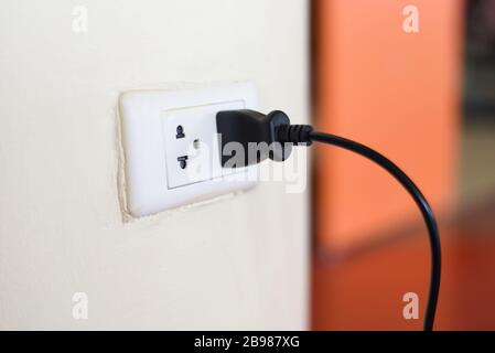 Home outlet plug is plugging socket on wall with black power cord cable / Power plug connecting electrical plug Stock Photo