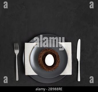 Easter minimal table setting with an egg nest on a black background. Space for text. Top view, flat lay. Stock Photo