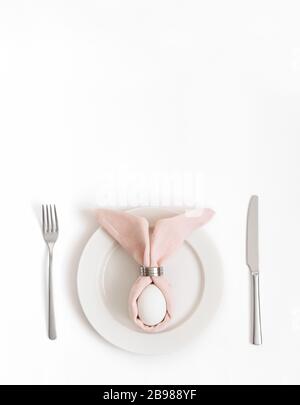 Easter table setting with egg in pink Easter bunny napkin on a white background. Vertical orientation. Copy space, top view, flat lay. Stock Photo