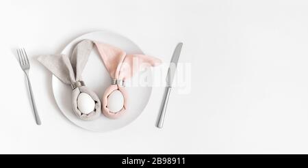 Happy easter concept. Easter table setting with egg in Easter bunny napkin on a white background. Banner. Copy space, top view, flat lay. Stock Photo