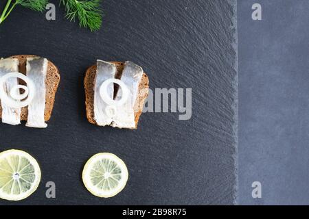 Sandwiches with pickled herring with onion rings and lemon. Healthy food. Black background. Stock Photo