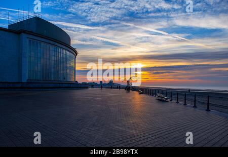 The waterfront promenade of Oostende (Ostend in English) at sunset with unrecognizable people silhouette walking by the beach, North Sea, Belgium. Stock Photo
