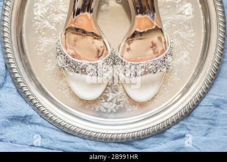 Sparkly white wedding shoes on silver platter with blue background Stock Photo