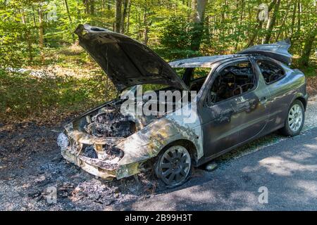 Burned car on the side of the road in the forrest in France Stock Photo