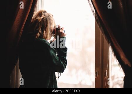 Young woman photographing with vintage camera through window while standing at home Stock Photo