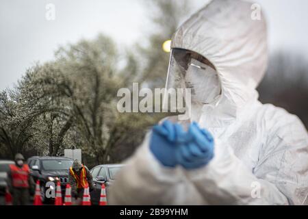 Holmdel, United States. 23rd Mar, 2020. A nurse changes out gloves while New Jersey National Guard Airmen direct traffic at a COVID-19 Community-Based Testing Site at the PNC Bank Arts Center in Holmdel, N.J., on March 23, 2020. The testing site, established in partnership with the Federal Emergency Management Agency, is staffed by the New Jersey Department of Health, the New Jersey State Police, and the New Jersey National Guard. This image was captured with a tilt-shift lens. Photo by Master Sgt. Matt Hecht/U.S. Air National Guard/UPI Credit: UPI/Alamy Live News Stock Photo