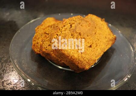 Three fresh slices of HomeMade Pumpkin Bread on clear glass plate on black kitchen countertop Stock Photo