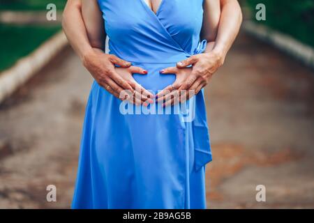 Pregnant woman and her husband holding hands on tummy in heart shape. Young loving family. New life concept Stock Photo