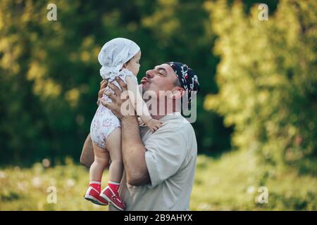 young grandfather playing with adorable baby girl over a nature background. Grandparents and grandchild leisure time concept. Stock Photo
