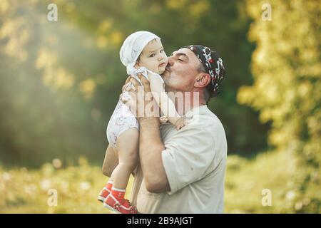 young grandfather playing with adorable baby girl over a nature background. Grandparents and grandchild leisure time concept. Stock Photo