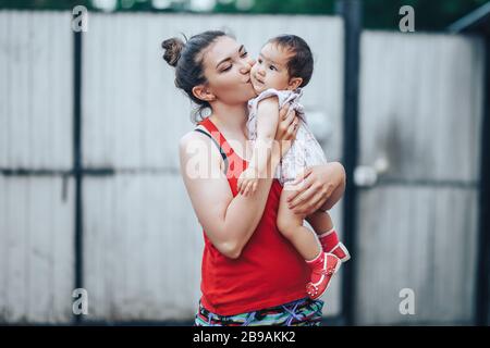 Beautiful Mother And Baby outdoors on the yard of house. Beauty Mum and her baby Child one year old playing in yard together. Mom and Baby