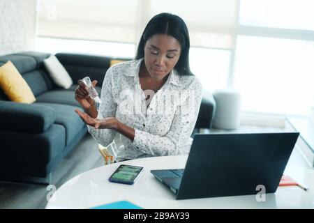 Black Woman Working From Home Using Hand Sanitizer Stock Photo