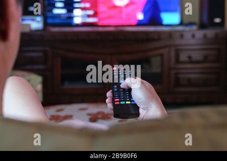 Man watching tv with focus on his hands on the remote control. Home entertainment or stay at home concept. Stock Photo