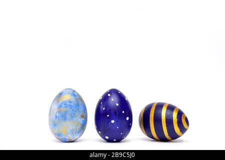 Three easter eggs trendy colored classic blue, white and golden decorated on white table. Happy Easter card with copy space for text. Minimal style Stock Photo