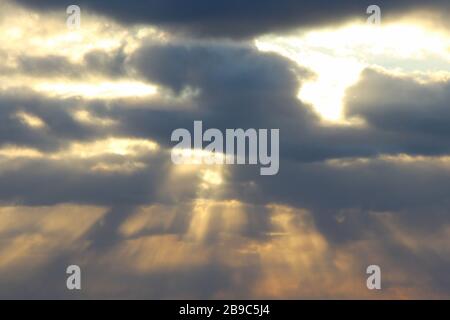The sun at sunset or dawn behind the clouds, shines through. The sun's rays in the sky. Stock Photo