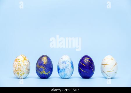 Five easter trendy colored classic blue and golden decorated eggs on blue background. Happy Easter card with copy space for text. Minimal easter style Stock Photo