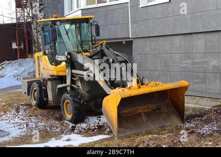 A black and yellow wheeled tractor stands against a wall of a house. Heavy construction machinery concept. Stock Photo