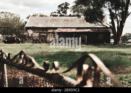 Old Stone Farmhouse in Disrepair Under Tree with Old Front Gate and Old Machinery Stock Photo