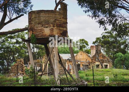 Old Stone Farmhouse in Disrepair with Rusty Old Water Tank Under Tree Stock Photo