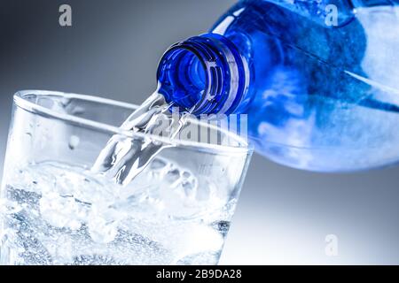 Pouring mineral water from blue bottle into clear glass on abstract grey background Stock Photo