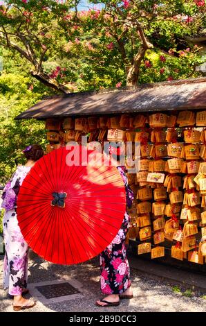 Two Japanese dressed with a yukata and umbrella. Engimono. Ema (Shinto) Wooden boards with wishes Stock Photo