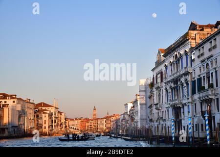 Looking down the Venetian canal during the golden hour of sunlight with at the same time a full moon in a blue sky Stock Photo