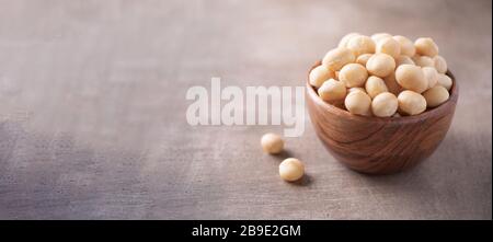 Macadamia nuts in wooden bowl on wood textured background. Copy space. Superfood, vegan, vegetarian food concept. Macro of macadamia nut texture, sele Stock Photo