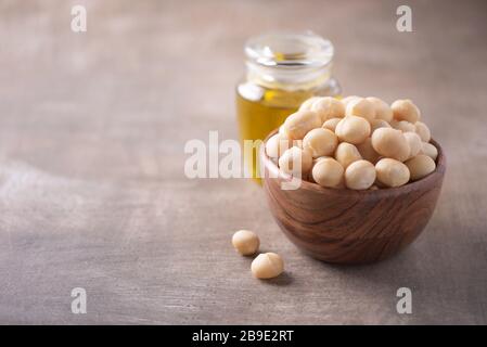 Macadamia nuts in wooden bowl and macadamia oil in bottle on wood textured background. Copy space. Superfood, vegan, vegetarian food concept. Macro of Stock Photo
