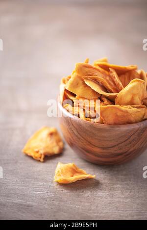 Dried mango in wooden bowl on wood textured background. Copy space. Superfood, vegan, vegetarian food concept. Macro of orange dried mango slices, sel Stock Photo