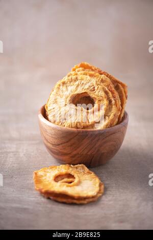 Slices of dried pineapple in wooden bowl on wood textured background. Copy space. Superfood, vegan, vegetarian food concept. Macro of pineapple textur Stock Photo