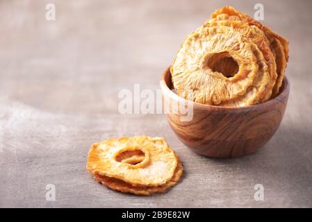 Slices of dried pineapple in wooden bowl on wood textured background. Copy space. Superfood, vegan, vegetarian food concept. Macro of pineapple textur Stock Photo