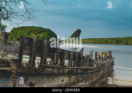 Very old and abandoned wooden boat in front of the Khao Khanab Nam mountains, mangroves forest and blue sky with rain clouds in Krabi town, Thailand Stock Photo